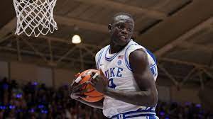 Khaman Maluach on stage at the NBA Draft, smiling in a suit lined with South Sudan and Uganda flags, holding his Phoenix Suns jersey beside Commissioner Adam Silver.