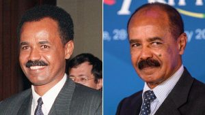 Eritrean President Isaias Afwerki standing at a podium during a national event, with a solemn crowd behind him.