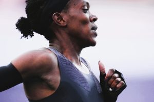 Faith Kipyegon sprinting in an aerodynamic skinsuit on a professional track, surrounded by pacemakers during her record-breaking mile attempt in Paris.