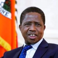 Mourners gathered around a framed photo of former Zambian president Edgar Lungu, with flags and flowers in the background. Zambia's president not wanted at predecessor's funeral, family says