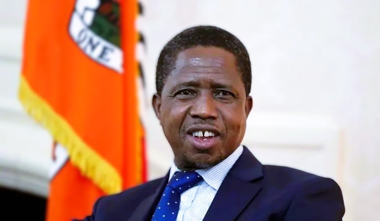 Mourners gathered around a framed photo of former Zambian president Edgar Lungu, with flags and flowers in the background. Zambia's president not wanted at predecessor's funeral, family says