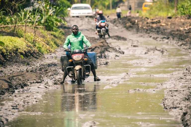 Flooded street in Kinshasa with submerged houses and stranded residents after heavy rainfall.