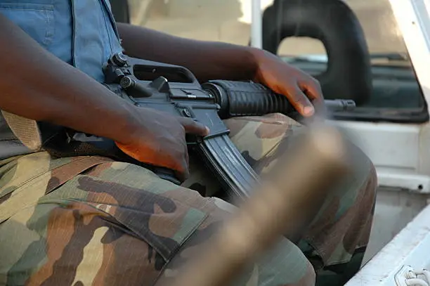 A South Sudanese soldier stands in formation near a dusty courtroom in Wau, symbolizing the intersection of military discipline and justice.