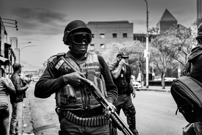 A group of Kenyan protesters holding tree branches and banners, surrounded by police officers in riot gear, during a tense demonstration in Nairobi.