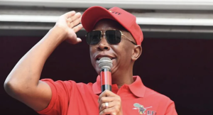 Julius Malema at a political rally, raising his fist while addressing a crowd of supporters.