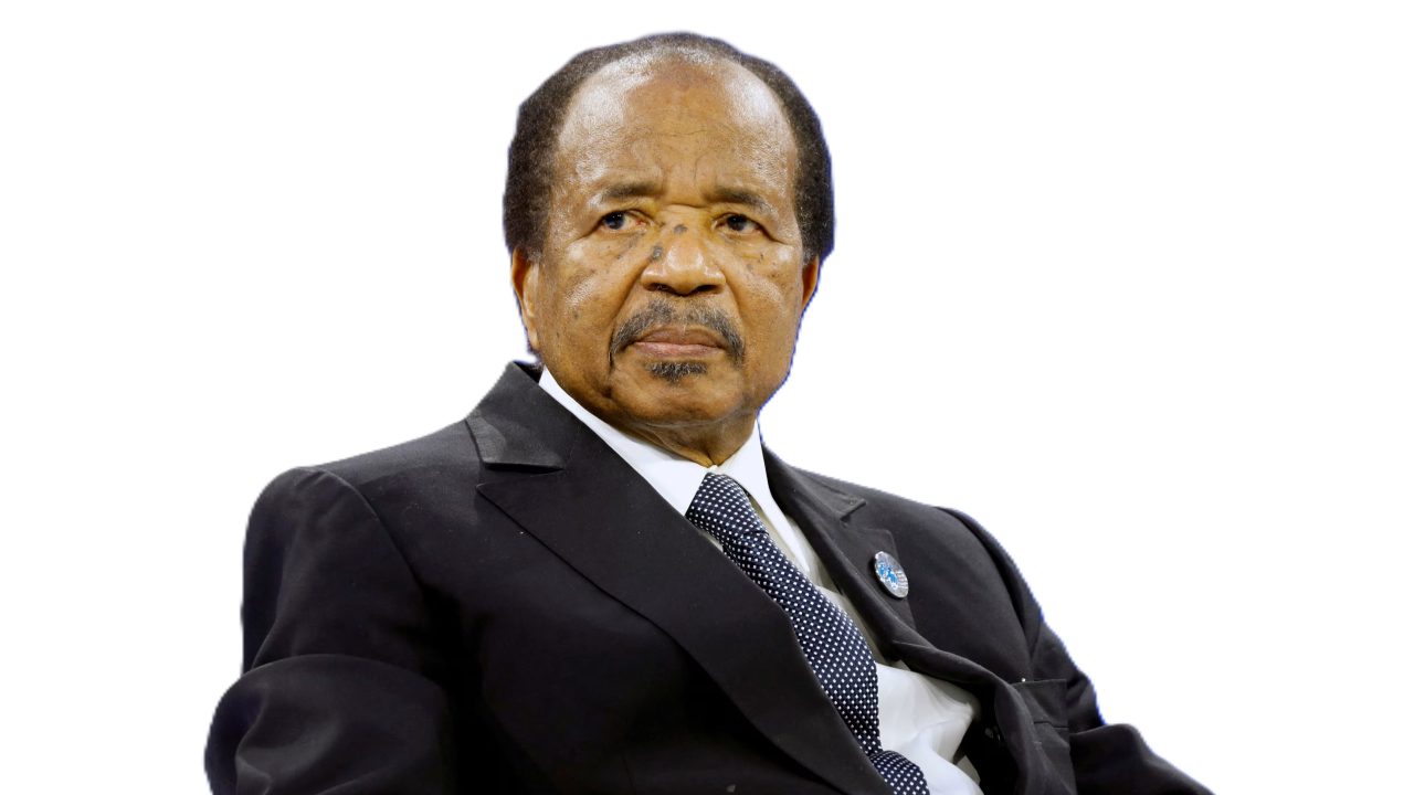 Cameroon President Paul Biya at a formal event, seated and wearing a dark suit with a stern expression.
