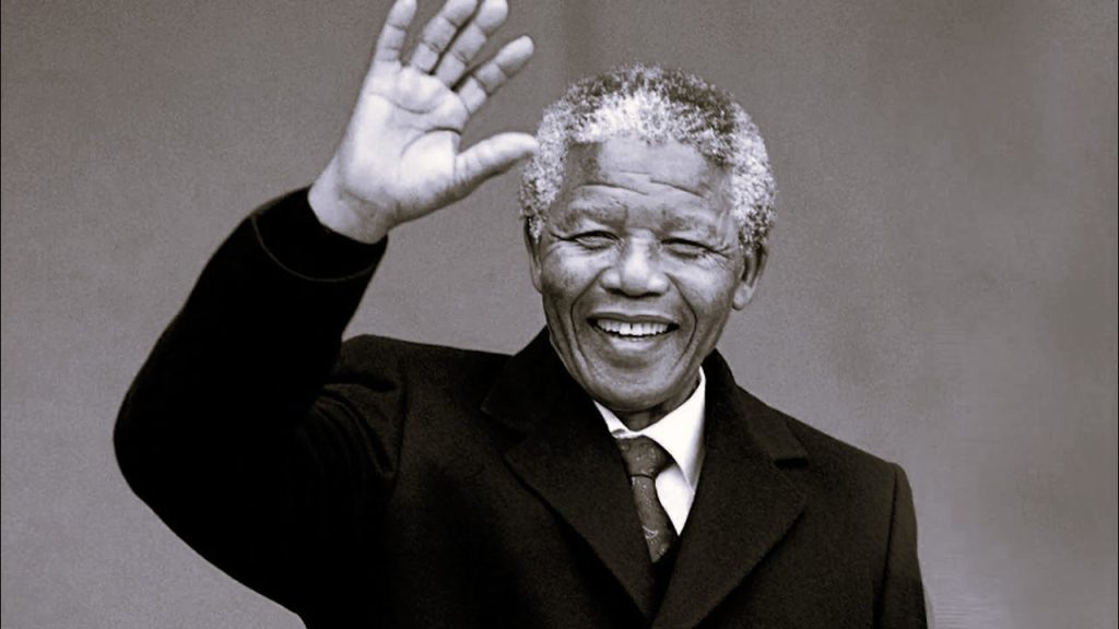 A tribute event held on Nelson Mandela International Day 2025, with people holding posters of Mandela and volunteering in community service, symbolizing global unity and the fight against poverty.