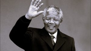 A tribute event held on Nelson Mandela International Day 2025, with people holding posters of Mandela and volunteering in community service, symbolizing global unity and the fight against poverty.