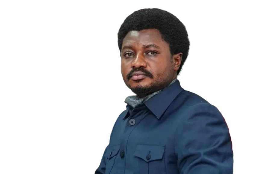 Constant Mutamba in a dark suit standing before a courtroom bench, speaking as journalists and court officials look on.