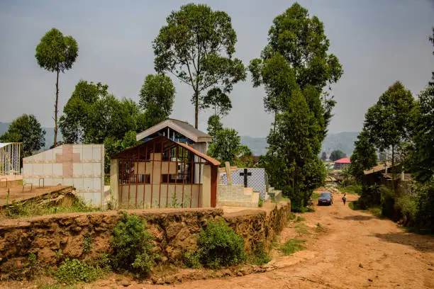 Scene showing aftermath of church attack in Komanda, DR Congo, with smoke rising from burned buildings and villagers mourning victims.