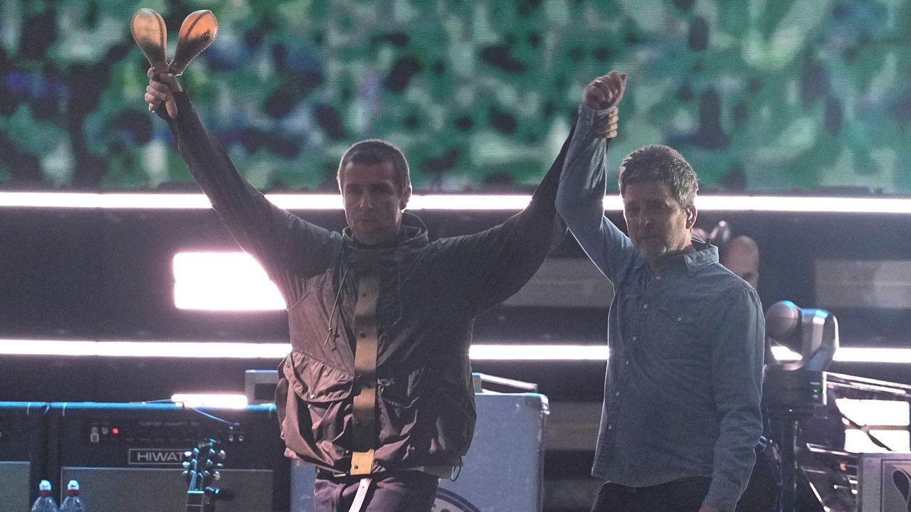 Liam and Noel Gallagher performing together on stage during Oasis’s 2025 reunion tour in Cardiff, with thousands of fans cheering in the background.